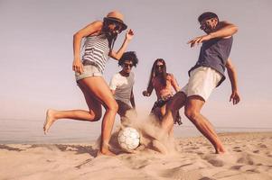 lustige zeit mit freunden. Gruppe fröhlicher junger Leute, die am Strand mit Fußball spielen foto