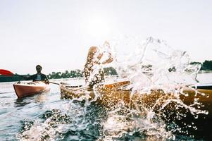 Sommertag am See genießen. junges Paar, das zusammen auf dem See Kajak fährt und Wasser spritzt foto