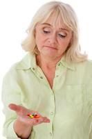 Pillen einnehmen. depressive Seniorin, die Pillen in der Hand hält und sie ansieht, während sie isoliert auf weißem Hintergrund steht foto