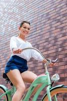 mit ihrem Oldtimer-Fahrrad. Tiefwinkelansicht einer attraktiven jungen lächelnden Frau, die ihr altes Fahrrad fährt foto