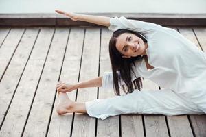 Dehnübungen im Freien. schöne junge lächelnde Frau in weißer Kleidung, die Yoga im Freien durchführt foto