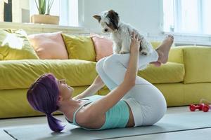 Selbstbewusste Frau in Sportkleidung, die zu Hause mit ihrem kleinen Hund trainiert foto