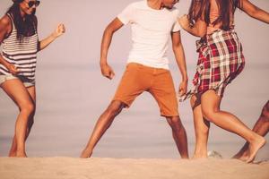 Spaß am Strand. Zugeschnittenes Bild von fröhlichen jungen Leuten, die am Strand mit Meer im Hintergrund mit Fußball spielen foto