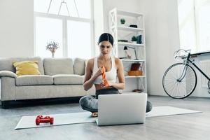 suchen, wie man Sport macht. Schöne junge Frau in Sportkleidung mit Laptop beim Training zu Hause foto