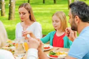 Gott für das Essen danken. familie, die hände hält und vor dem abendessen betet, während sie draußen am tisch sitzt foto