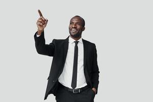 hübscher junger afrikanischer mann in formalwear, der kopienraum zeigt und lächelt, während er vor grauem hintergrund steht foto