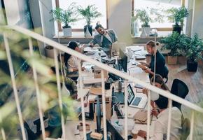 Draufsicht auf junge moderne Menschen in eleganter Freizeitkleidung, die bei der Arbeit im Büro mit modernen Technologien kommunizieren und diese nutzen foto