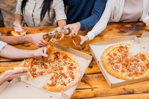 Prost auf dieses Wochenende Draufsicht einer Gruppe junger Leute, die Flaschen mit Bier halten und Pizza essen, während sie im Freien stehen foto