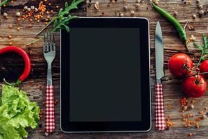 Was wir heute bekommen haben Draufsicht auf das digitale Tablet, das auf dem hölzernen Esstisch mit Gemüse liegt foto