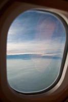 Wolken und Himmel durch das Fenster eines Flugzeugs gesehen