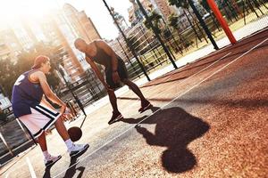 bereit zu schlagen. Zwei junge Männer in Sportkleidung spielen Basketball und verbringen Zeit im Freien foto