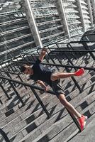auf der Treppe trainieren. voller Länge des jungen Mannes in Sportkleidung springen, während er draußen trainiert foto