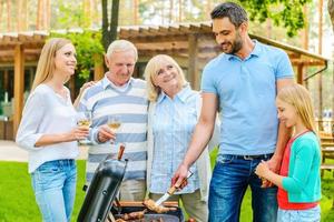 Familiengrillen. Glückliche fünfköpfige Familie, die Fleisch auf dem Grill auf dem Hinterhof ihres Hauses grillt foto