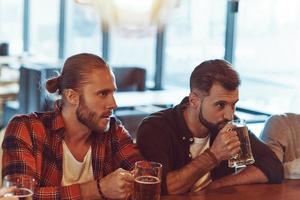 Junge Männer in Freizeitkleidung genießen Bier, während sie zusammen in der Kneipe sitzen foto