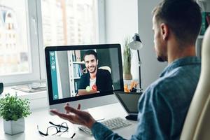 Selbstbewusster junger Mann, der im Büro per Videoanruf mit einem Kollegen spricht foto