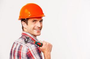 Handwerker mit Schraubenschlüssel. Rückansicht eines hübschen jungen Heimwerkers mit Schlüssel auf der Schulter und Blick über die Schulter, während er vor grauem Hintergrund steht foto