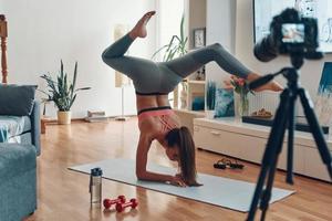 flexible junge frau in sportkleidung, die auf händen steht, während sie social-media-videos macht foto