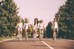 zusammen einen schönen sommertag genießen. Gruppe junger Leute, die Fahrräder entlang einer Straße fahren und glücklich aussehen foto