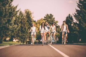 Radfahren mit Spaß. Gruppe junger Leute, die Fahrräder entlang einer Straße fahren und glücklich aussehen foto
