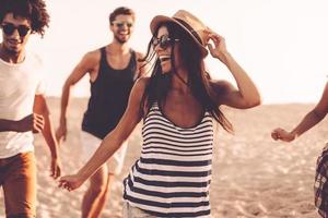 Jugend und Freiheit genießen. Gruppe junger, fröhlicher Menschen, die am Strand entlang laufen und glücklich aussehen foto