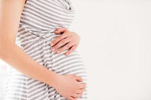 Schwangerschaft. Seitenansicht Zugeschnittenes Bild einer schwangeren Frau, die die Hände auf ihrem Bauch hält foto