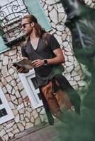moderner Tourist. hübscher junger Mann in Freizeitkleidung, der Karte hält und wegschaut, während er im Freien steht foto
