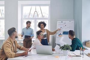 gruppe selbstbewusster junger leute in eleganter freizeitkleidung, die über geschäfte diskutieren, während sie sich im büro treffen foto