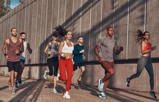 Volle Länge von Menschen in Sportkleidung, die beim Training auf dem Bürgersteig im Freien joggen