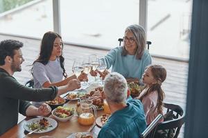 glückliche Familie mit mehreren Generationen, die beim gemeinsamen Abendessen anstößt und lächelt foto