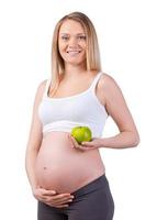 schwangere Frau mit Apfel. schöne schwangere Frau, die grünen Apfel hält und lächelt, während sie isoliert auf weiß steht foto
