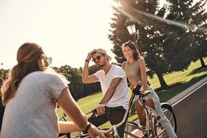Fahrradfreunde. Gruppe glücklicher junger Menschen in Freizeitkleidung, die lächeln und kommunizieren, während sie gemeinsam im Freien radeln foto