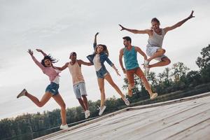 Sommerspaß. in voller Länge von jungen Leuten in Freizeitkleidung, die lächeln und gestikulieren, während sie auf den Pier springen foto