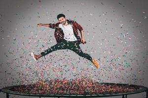 unbeschwerter Spaß. Luftaufnahme eines gutaussehenden jungen Mannes, der mit Konfetti um ihn herum auf Trampolin springt foto