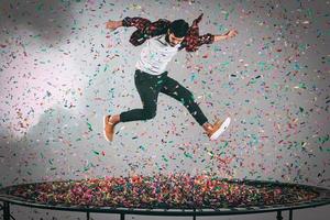 bunter Spaß. Luftaufnahme eines gutaussehenden jungen Mannes, der auf Trampolin springt, mit Konfetti um ihn herum foto