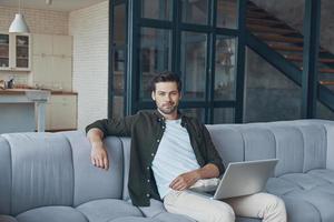 hübscher junger mann, der laptop verwendet, während er zu hause auf dem sofa sitzt foto