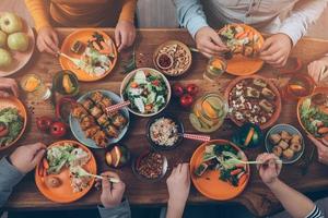 Abendessen mit Freunden genießen. Blick von oben auf eine Gruppe von Menschen, die zusammen zu Abend essen, während sie am rustikalen Holztisch sitzen foto