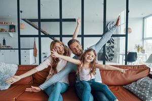 Verspielte junge Familie, die ihre Hände ausstreckt und in die Kamera schaut, während sie sich zu Hause verbindet foto