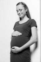 schwangere Frau. Schwarz-Weiß-Bild einer schönen jungen schwangeren Frau, die ihren Bauch berührt und ihn mit einem Lächeln betrachtet foto