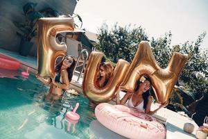 Attraktive junge Frauen in Badebekleidung lächeln und heben Luftballons hoch, während sie draußen im Pool stehen foto