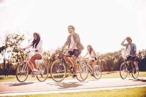 Qualitätszeit miteinander verbringen. Gruppe junger Leute, die Fahrräder entlang einer Straße fahren und glücklich aussehen foto