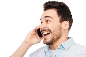 freudige Kommunikation. Porträt eines fröhlichen jungen Mannes, der auf dem Handy spricht und im Stehen vor weißem Hintergrund lächelt foto