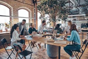 Gruppe junger moderner Menschen in eleganter Freizeitkleidung, die bei der Arbeit im Büro kommunizieren und moderne Technologien nutzen foto