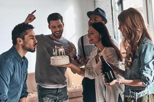 beeil dich, dir etwas zu wünschen. glücklicher junger mann, der kerzen bläst, während er geburtstag unter freunden feiert foto