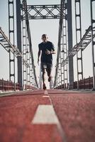 morgens joggen. Volle Länge des jungen afrikanischen Mannes in Sportkleidung, der beim Joggen auf der Brücke im Freien trainiert foto