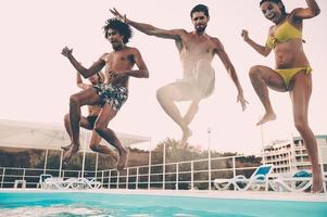 in den Pool springen. Gruppe schöner junger Leute, die glücklich aussehen, während sie gemeinsam ins Schwimmbad springen foto