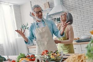 Fröhliches Seniorenpaar bereitet sich darauf vor, ein Abendessen zu kochen und lächelt, während es Zeit zu Hause verbringt foto