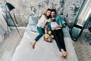 fröhliches Selfie. Blick von oben auf ein schönes junges Paar, das sich selbst macht und lächelt, während es zu Hause Zeit im Bett verbringt foto