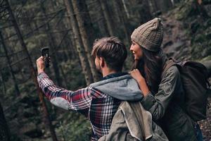den Moment festhalten. Schönes junges Paar, das sich beim gemeinsamen Wandern im Wald selbst macht foto