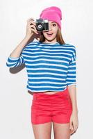 Lächeln Sie verspielte junge Frau in funky Kleidung, die durch eine Kamera schaut, während sie vor weißem Hintergrund steht foto