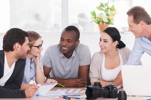 freundliches Bürogespräch. Gruppe fröhlicher Geschäftsleute, die zusammen am Tisch sitzen und etwas besprechen foto